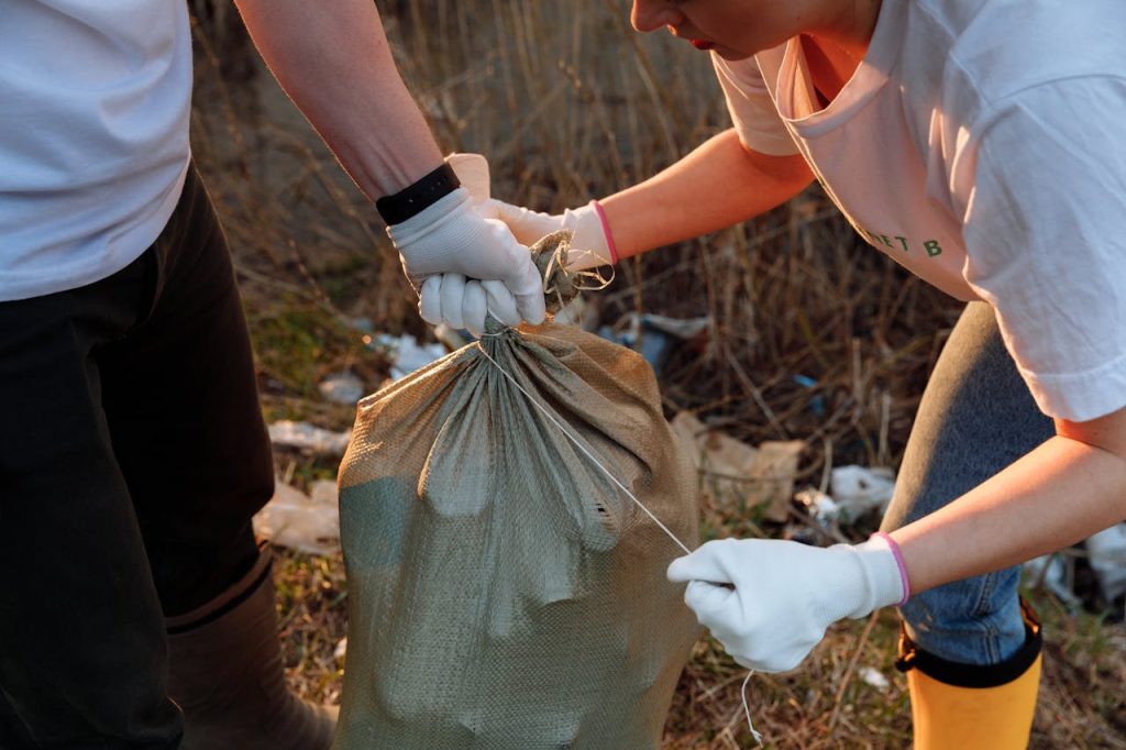 a-person-tying-a-sack-7656990 Two people tying a sack of garbage during an outdoor community cleanup activity.